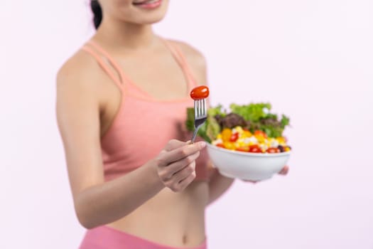 Young sporty Asian woman in sportswear holding salad bowl fill with vibrant of fruit and vegetable. Natural youthful and fit body lifestyle with balance nutrition on isolated background. Vigorous