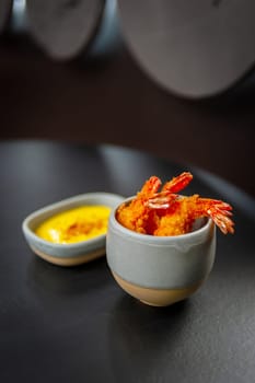 Tempura deep-fried shrimp with spiced sauce on a plate on a dark background. Appetizer in the style of Japanese cuisine. High quality photo.