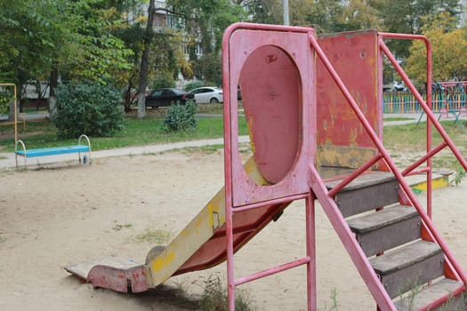 An old playground with a pink metal slide . Sand covering of the playground.