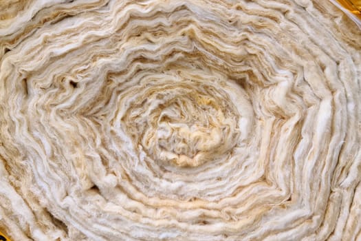 A roll of new twisted glass wool, a soft material for insulating walls and other structures, close-up, background.