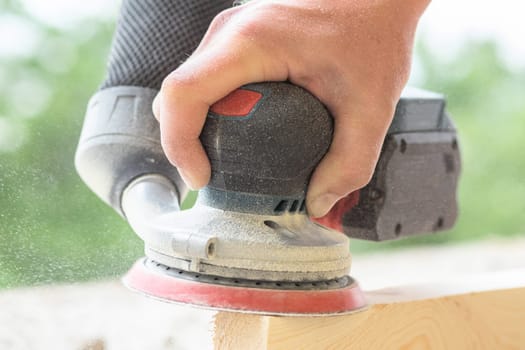 An eccentric sander in the hands of a worker grinds a wooden surface, close-up.