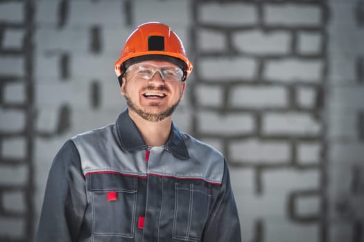 Portrait of a happy smiling bearded Caucasian worker in overalls, safety helmet and safety glasses at a construction site.