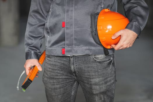 Construction level tool, safety glasses and protection helmet in the hand of a construction worker in overall. DIY or home renovation concept.