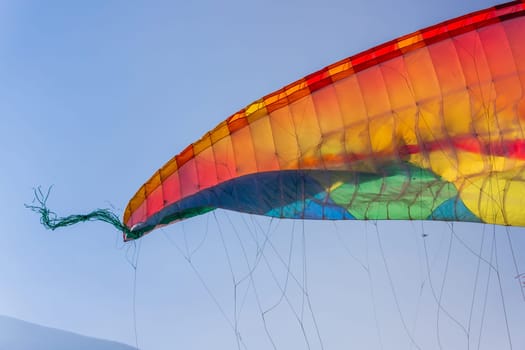 Close-up on part of the wing of a multi-colored paraglider against a blue sky.