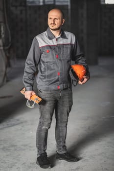 Construction worker in overalls, with a helmet, a construction level and safety glasses in his hands, is ready for his shift. Professional at work.