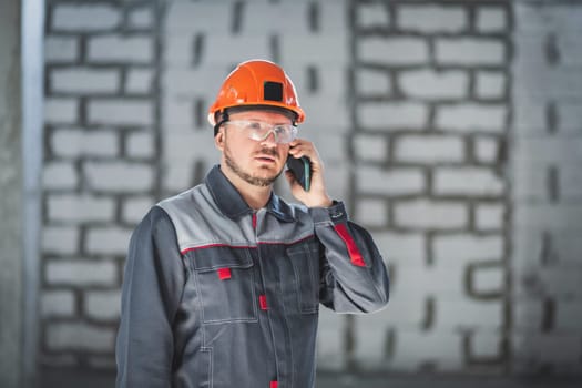 Caucasian male builder in overalls and helmet speaks on a cell phone.