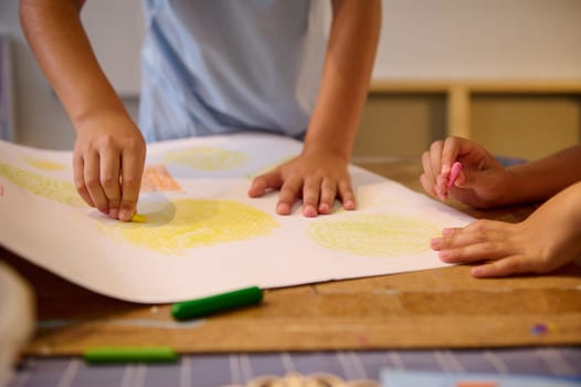 Close-up kids hand holding pencils and drawing on white paper sheet in creative art workshop. Creativity and art skills development concept. Kids and education