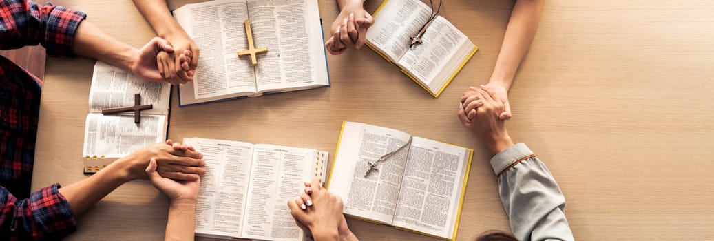 Cropped image of group of people praying together while holding hand on holy bible book at wooden church. Concept of hope, religion, faith, christianity and god blessing. Top view. Burgeoning.