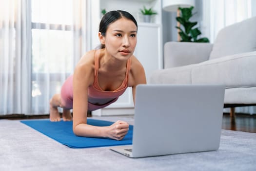 Fit young asian woman planing on the living room floor while following exercise instruction on online training video. Healthy lifestyle workout routine at home. Balance and endurance concept. Vigorous