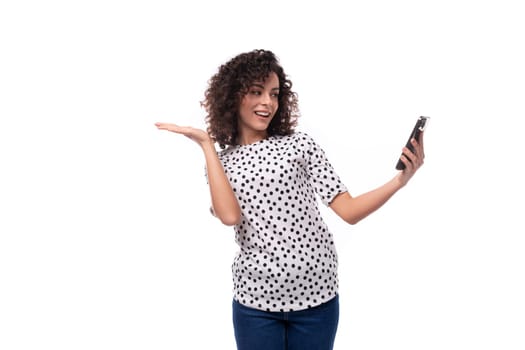 a slender young stylish woman with a curly haircut dressed in a blouse with polka dots speaks on a video call on the phone.