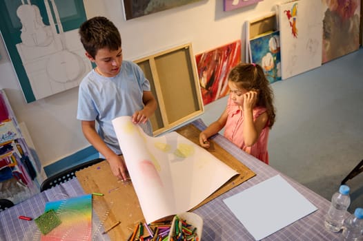 View from above of two Caucasian cute kids drawing in creative art workshop. Learning. Painting. Kids education and entertainment. Development of artistic skills in creative art studio or art gallery