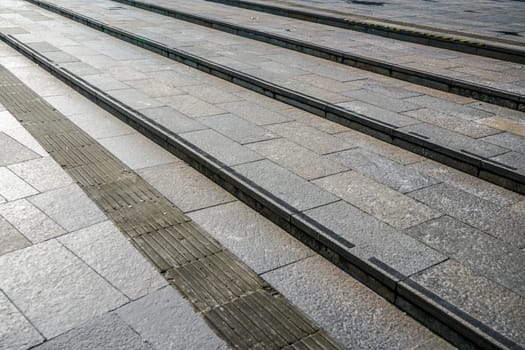 Sun shines on pavement made of stone tiles, divided by small canals for rain water. Abstract urban background with diagonal lines