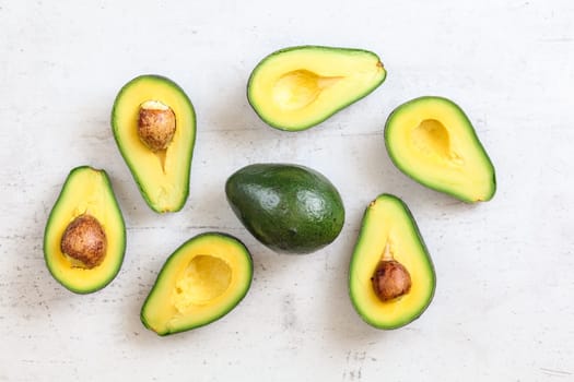 Overhead shot - avocados halves, some with seed, whole green pear in middle, on white working board.