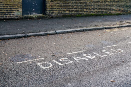 Word DISABLED written on asphalt near reserved parking space at street in outer London