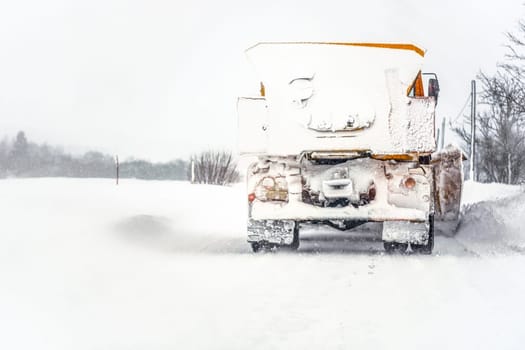 Orange plough truck on path completely covered with snow, gray sky and trees in background, view from back car driving behind - winter road maintenance