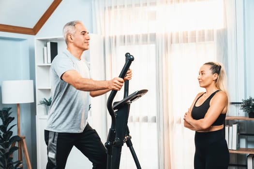 Active senior couple running on elliptical running machine at home together as fitness healthy lifestyle and body care after retirement for pensioner. Clout