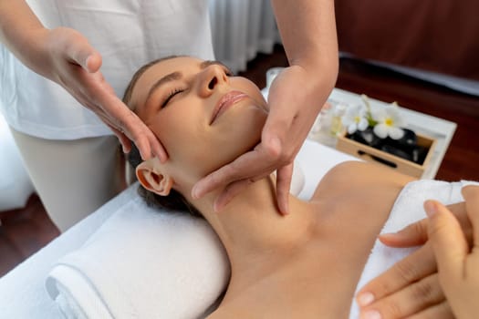 Caucasian woman enjoying relaxing anti-stress head massage and pampering facial beauty skin recreation leisure in dayspa modern light ambient at luxury resort or hotel spa salon. Quiescent