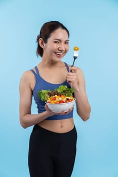 Young sporty Asian woman in sportswear holding salad bowl fill with vibrant of fruit and vegetable. Natural youthful and fit body lifestyle with balance nutrition on isolated background. Vigorous