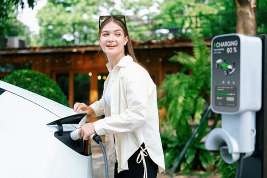 Young woman and sustainable urban commute with EV electric car recharging at outdoor cafe in springtime garden, green city sustainability and environmental friendly EV car. Expedient