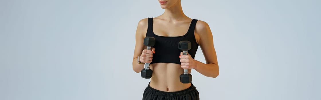 Woman doing exercises with dumbbells for hands training on studio background . Healthy lifestyle