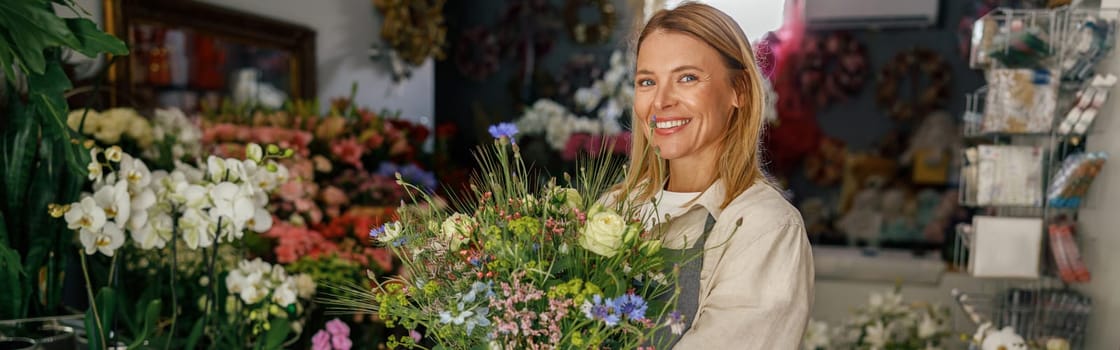 Attractive woman flower shop owner in apron holding bouquet of flowers at florist store