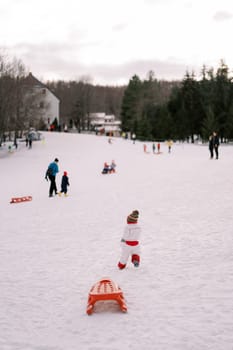 Small child in overalls drags a sled along a rope on a hill. Back view. High quality photo