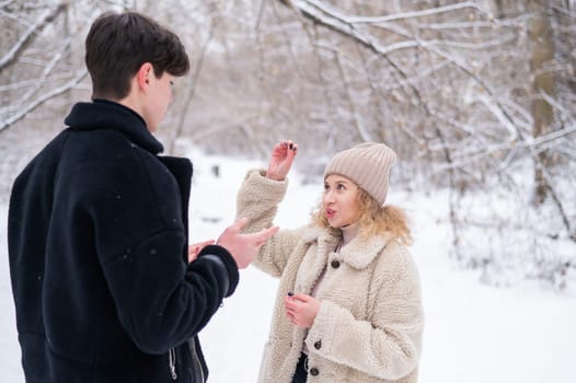 A young couple walks in the winter in the forest. Deaf Guy and a girl communicate using gestures outdoors