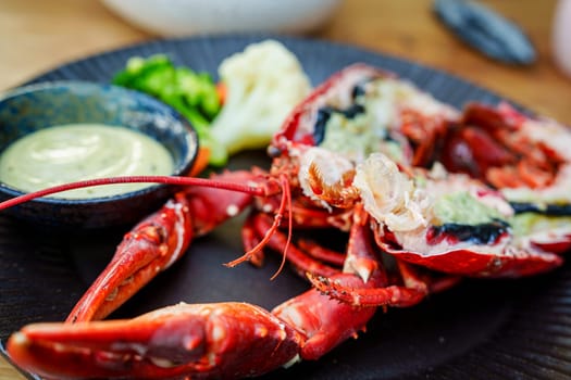 Sumptuous boiled red lobster halves, cooked to perfection and elegantly presented on a sophisticated black plate, served at a reputable seafood restaurant.