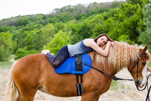 young woman doing yoga on a horse against the backdrop of trees.