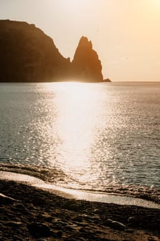 A red burning sunset with the silhouette of a cliff over the sea. Abstract nature summer or spring ocean sea background. Small waves on golden warm water surface with bokeh lights from sun.