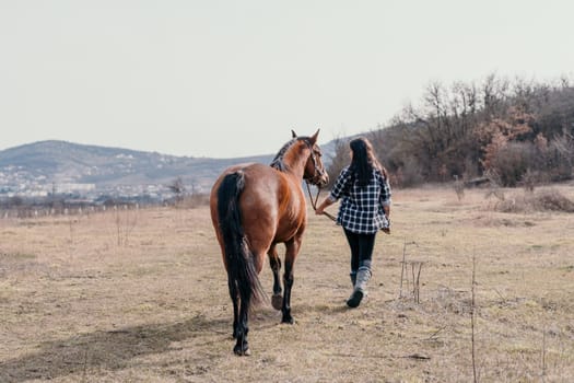 Cute happy young woman with horse. Rider female drives her horse in nature on evening sunset light background. Concept of outdoor riding, sports and recreation.