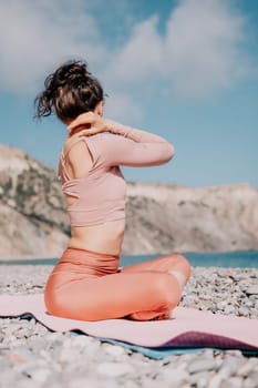 Young woman with long hair in white swimsuit and boho style braclets practicing outdoors on yoga mat by the sea on a sunset. Women's yoga fitness routine. Healthy lifestyle, harmony and meditation