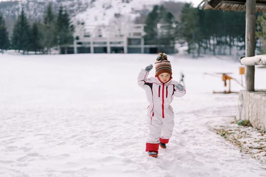 Little girl walks through the snow on a hill with her hands up. High quality photo