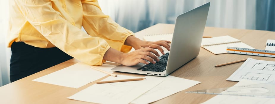 Professional architect working on laptop at modern office on working table with architectural equipment and blueprint scatter around. Living and design concept. Focus on hand. Closeup. Delineation.