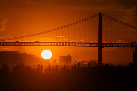 The sun is setting behind a suspension bridge