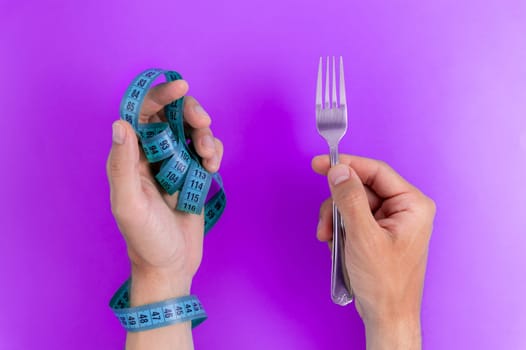 Diet concept, measuring tape, weight loss. Diet concept. Hand holding fork with tape measure on color background.