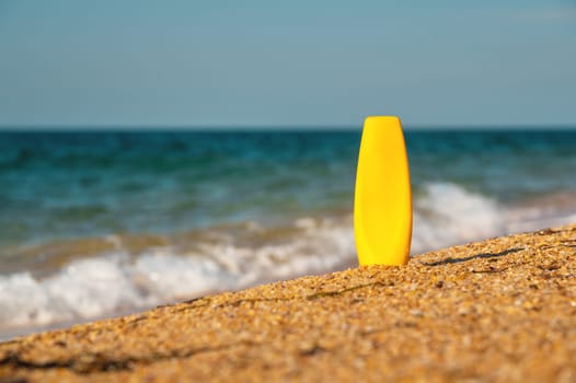 A bottle of sunscreen on the sand against the background of the sea. Yellow tube of sunscreen on the beach close-up. Sun protection cosmetics concept