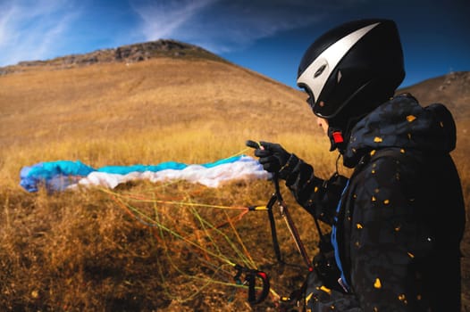 A paraglider lands or rises on the yellow grass on a sunny day. A man after or before a paragliding flight. Glider with parachute, wide angle rear view
