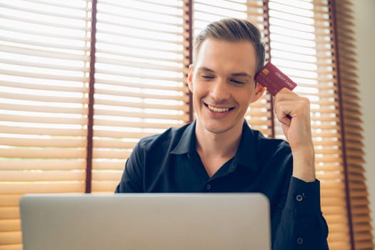 Young man using laptop with credit card for internet banking, online shopping E commerce by online payment gateway at home office. Modern and convenience online purchasing with debit card. Unveiling