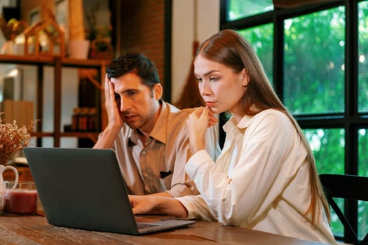 Young couple working remotely on laptop in cafe look tired and frustrated. Digital nomad freelancers or college students struggling to meet a deadline overwhelmed by workload. Expedient