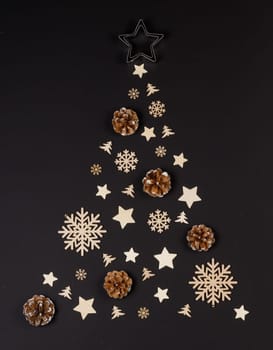 Christmas Tree made of wooden decor and pine cones on black paper background. Christmas Holiday Concept. Flat Lay