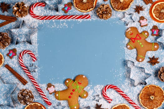 Christmas food gingerbread cookie caramel candy cane cinnamon mold shape anise orange slice on blue background with copy space