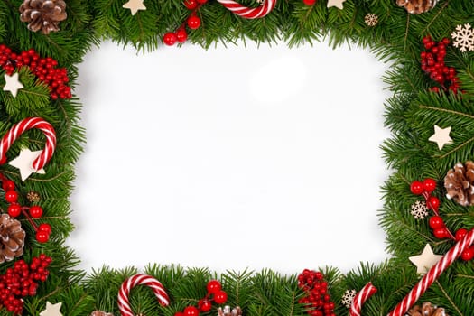 Christmas Border frame of tree branches around white background with copy space isolated, red decor, berries, stars, cones, candy canes