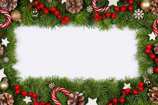 Christmas Border frame of tree branches on white background with copy space isolated, red and white decor, berries, stars, cones