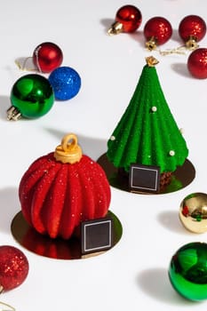Colorful sparkling Christmas tree toys and pastries in shape of red ball and green festive spruce decorated with sugar drops on white surface. Collection of delicious handmade holiday desserts