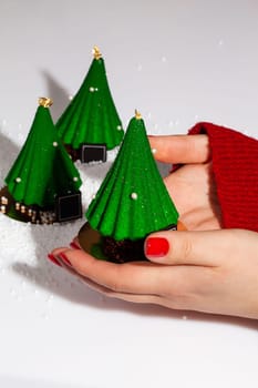 Female hands holding green glazed Christmas tree shaped dessert decorated with golden topper and sugar beads. Delicious treats for New Year celebration. Creating festive mood concept