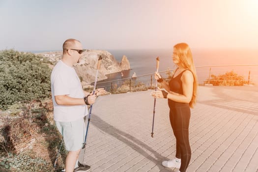 Happy Middle aged couple or friends practicing nordic walking in park near sea. Mature couple with trekking poles walking, practicing Nordic walking outdoors. Aging youthfully and sport concept.