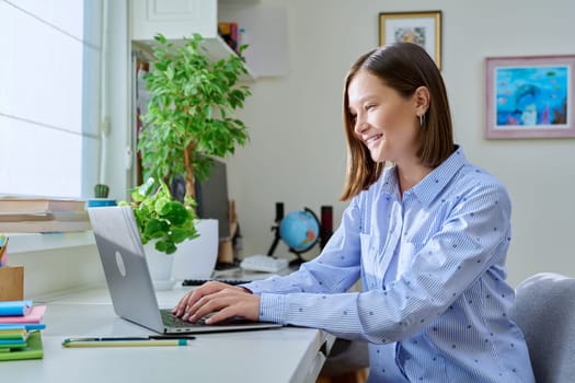 Young smiling woman typing on laptop computer at home. Female freelancer, an employee working remotely, university student studying online preparing for exams. Technology youth training education work