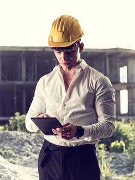 A man wearing a hard hat and holding a tablet in costruction site