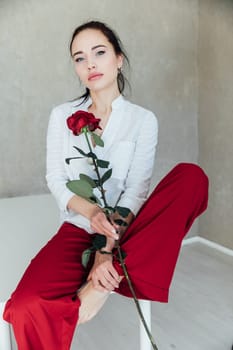 woman with a rose in red pants sits on a table in the room